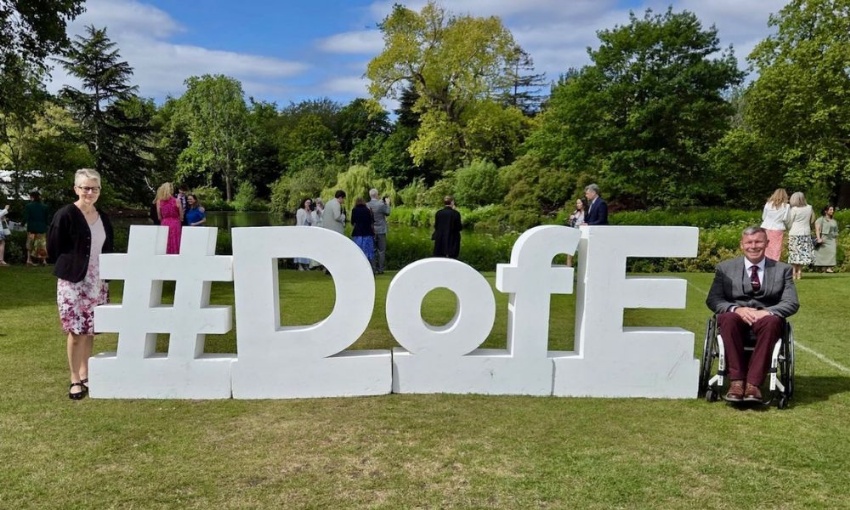 Guests posing beside a large #DofE sign in the Buckingham Palace gardens during the DofE 70th anniversary celebration.